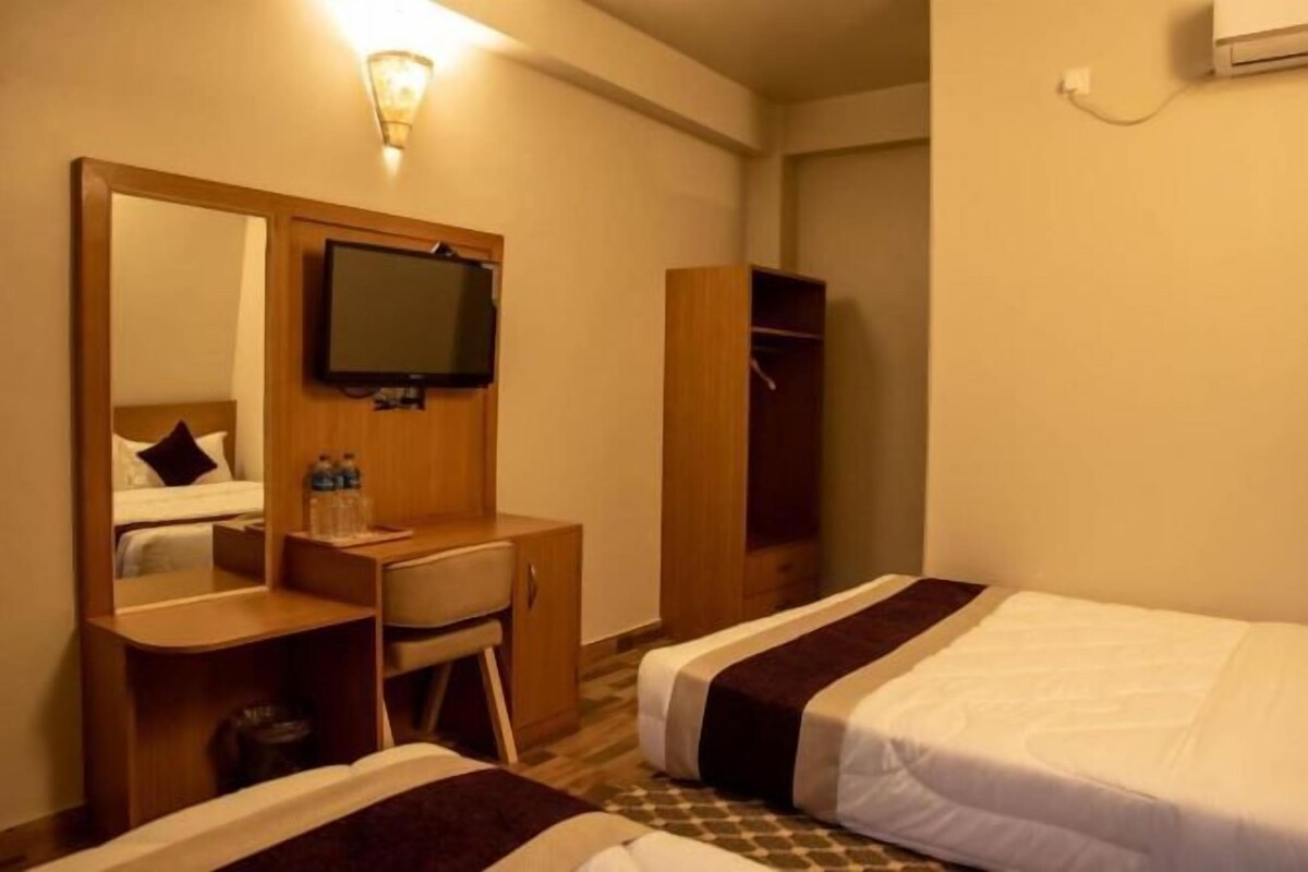 A hotel room with a bed, a desk with a chair, a mirror, a television, and a wardrobe.