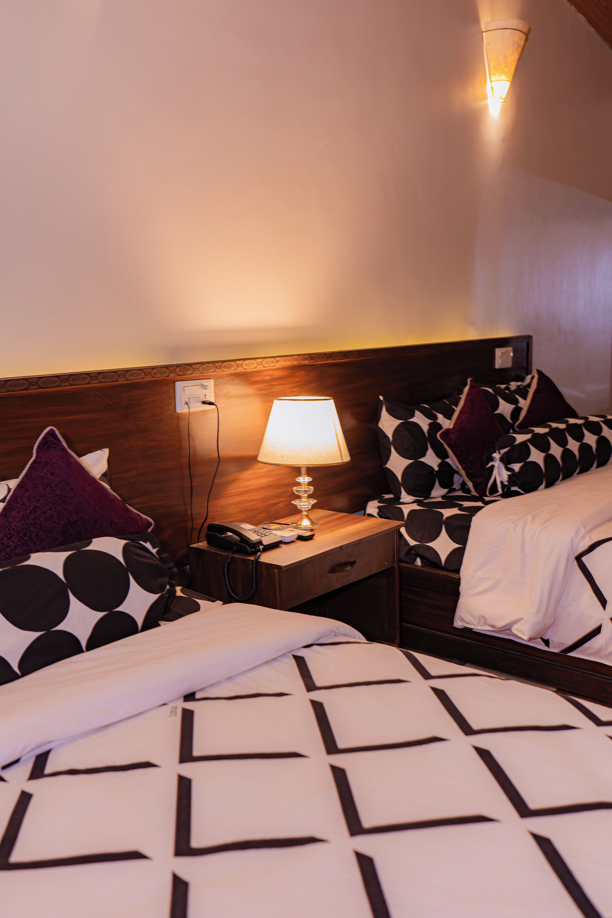 Habitación de hotel con dos camas, cada una con ropa de cama estampada, una mesita de noche con lámpara, y una lámpara de pared.