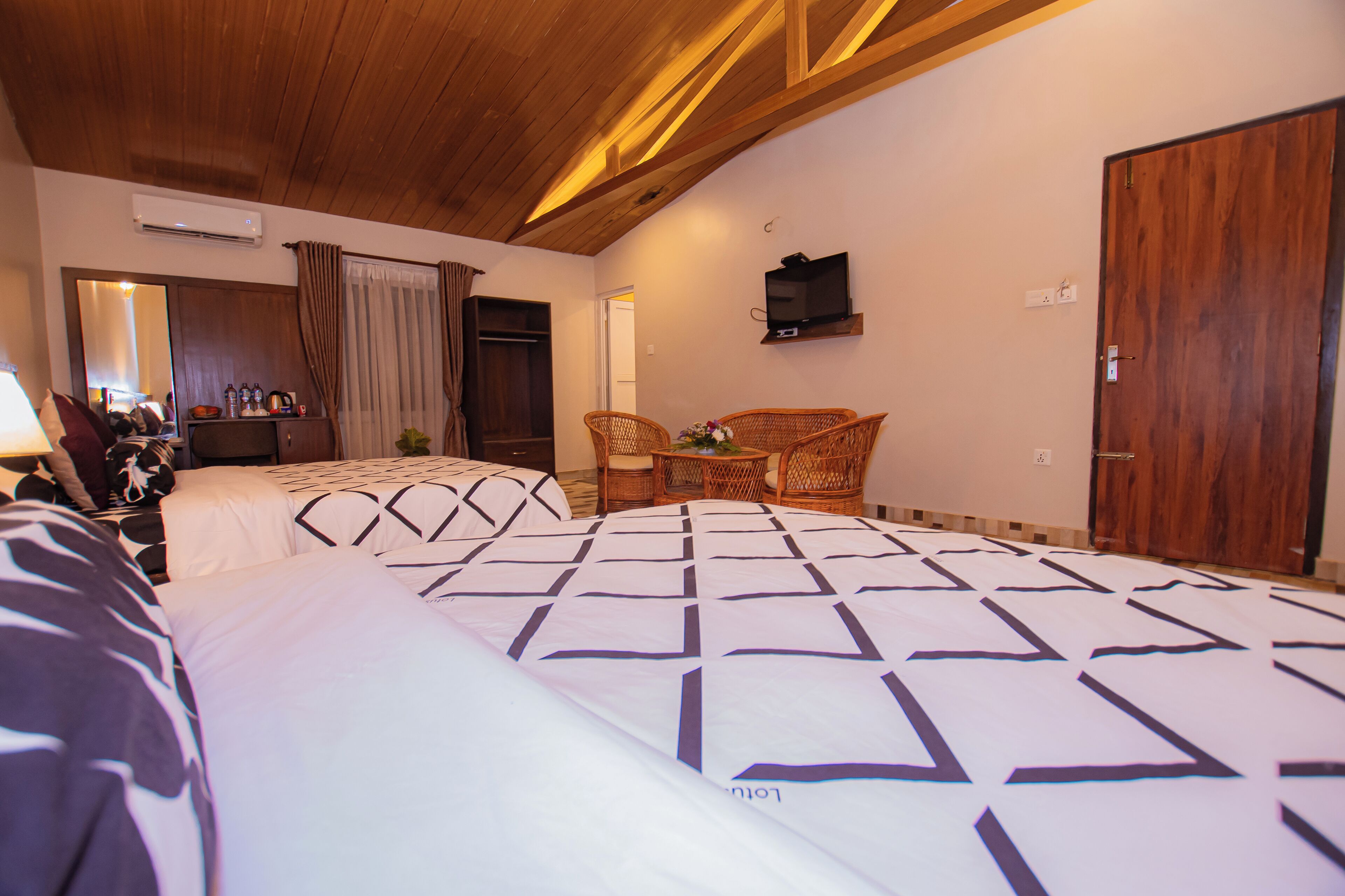 Habitación de hotel con dos camas, televisor, techo de madera y armario.