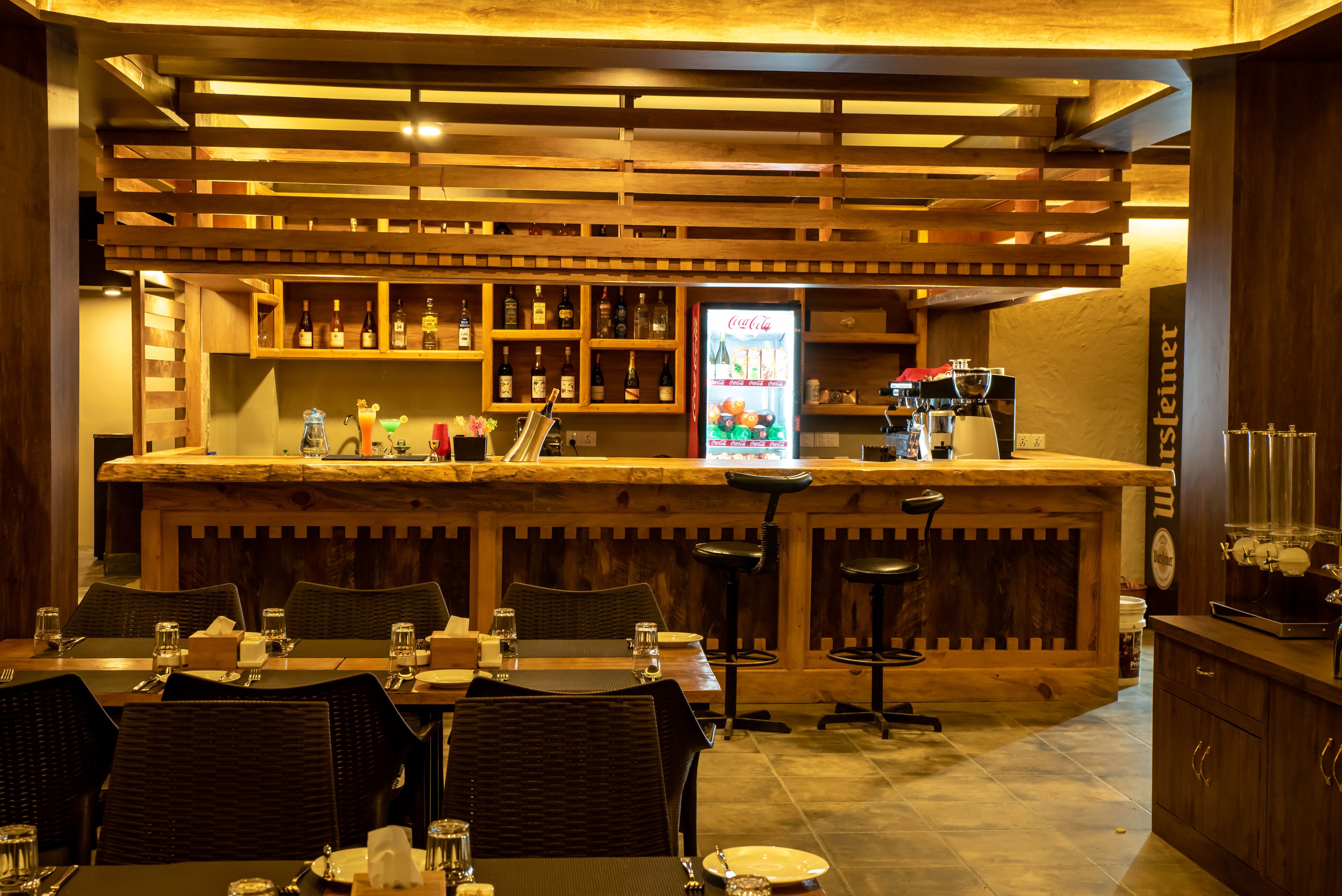 A bar area with wooden shelves, a refrigerator, and bar stools.