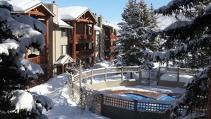 Une station de ski enneigée, avec des bâtiments en bois, une piscine et un paysage hivernal.