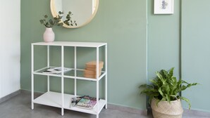 A white console table with shelves, a round mirror, and framed artwork on a green wall. - AirTLV Comfortable 3 BDRM in Old North (Tel Aviv)