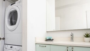 A laundry room with two stacked washing machines and a sink with a mirror above it. - AirTLV Comfortable 3 BDRM in Old North (Tel Aviv)