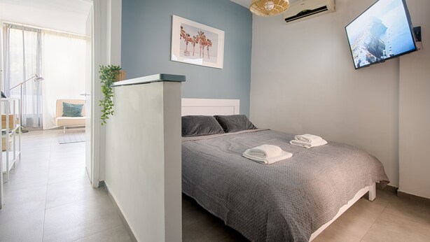 A bedroom with a bed, a TV, a wall-mounted air conditioner, and a framed picture on the wall. - AirTLV Comfortable 3 BDRM in Old North (Tel Aviv)