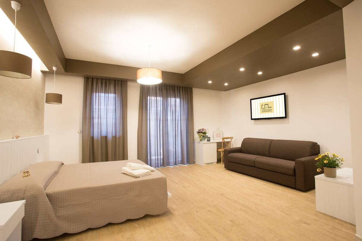 Una habitación de hotel moderna con una cama, un sofá, un escritorio y una planta en maceta.
