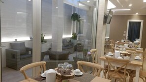 A modern dining area with glass partitions, wooden furniture, and a view of a cozy seating area with sofas and potted plants. - B&B L'Abbazia (Torremaggiore)