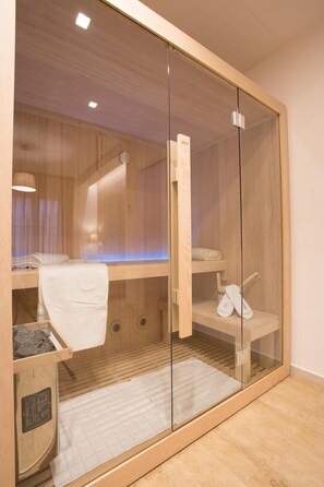 A modern sauna room with wooden walls and a glass partition. There is a bench with towels and a small shelf with personal items. - B&B L'Abbazia (Torremaggiore)