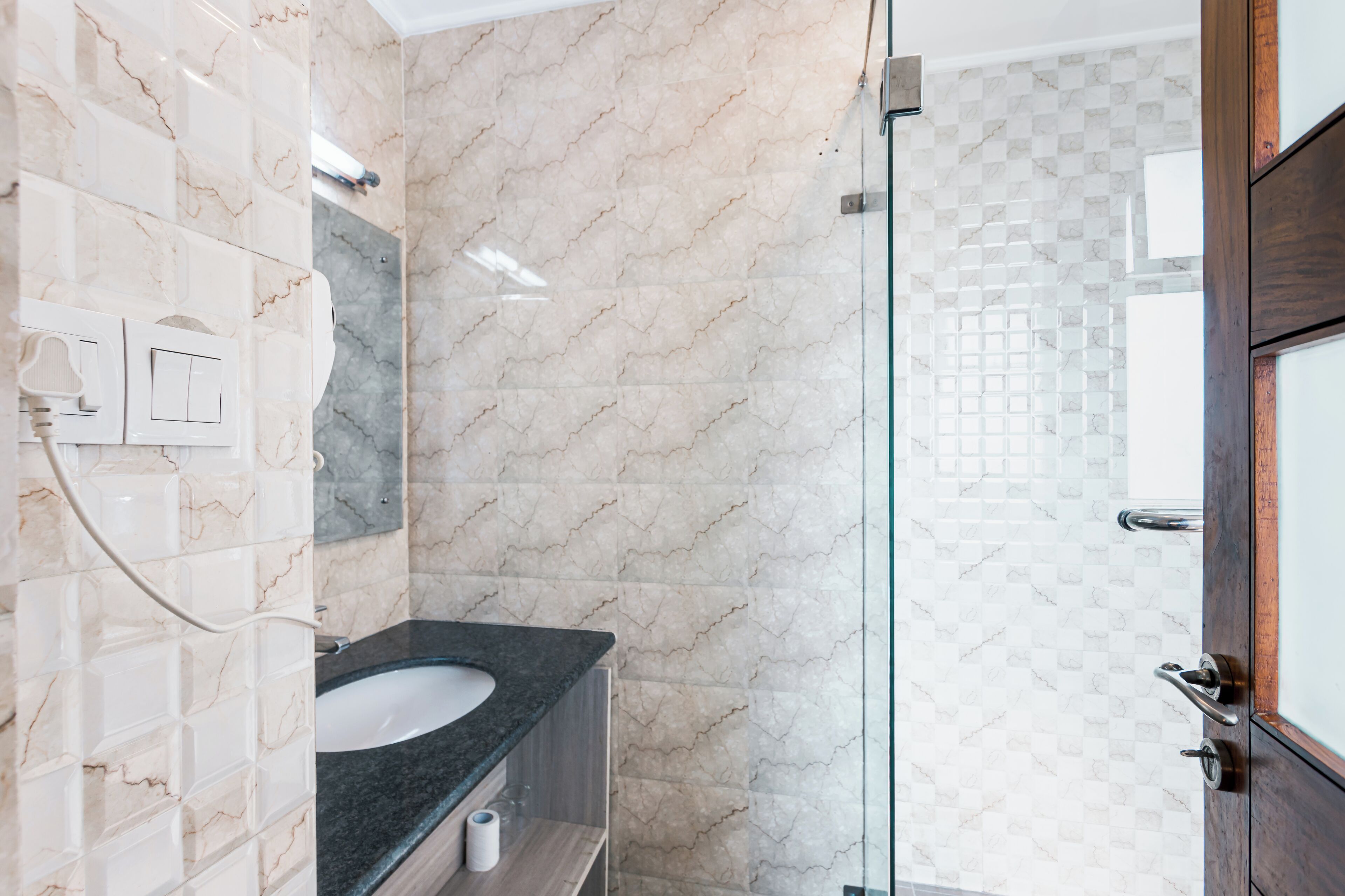A bathroom with a marble wall, a sink, and a glass shower enclosure.