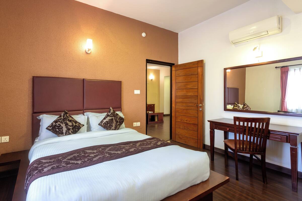 Habitación de hotel con cama, escritorio, silla, espejo y aire acondicionado.