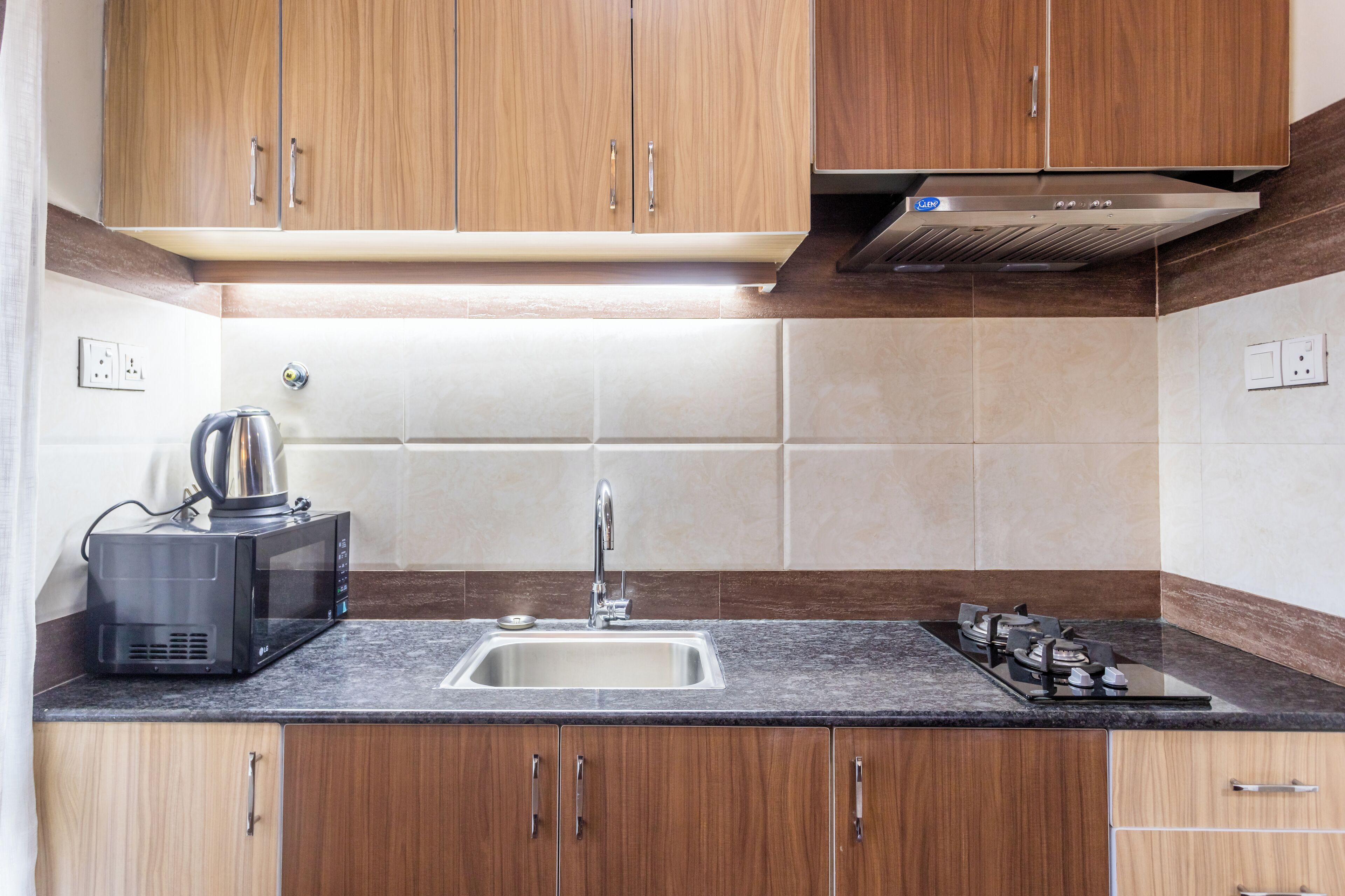 Una cocina con armarios de madera, un lavamanos de acero inoxidable, un microondas y una estufa a gas.