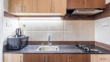 Una cocina con armarios de madera, un lavamanos de acero inoxidable, un microondas y una estufa a gas.