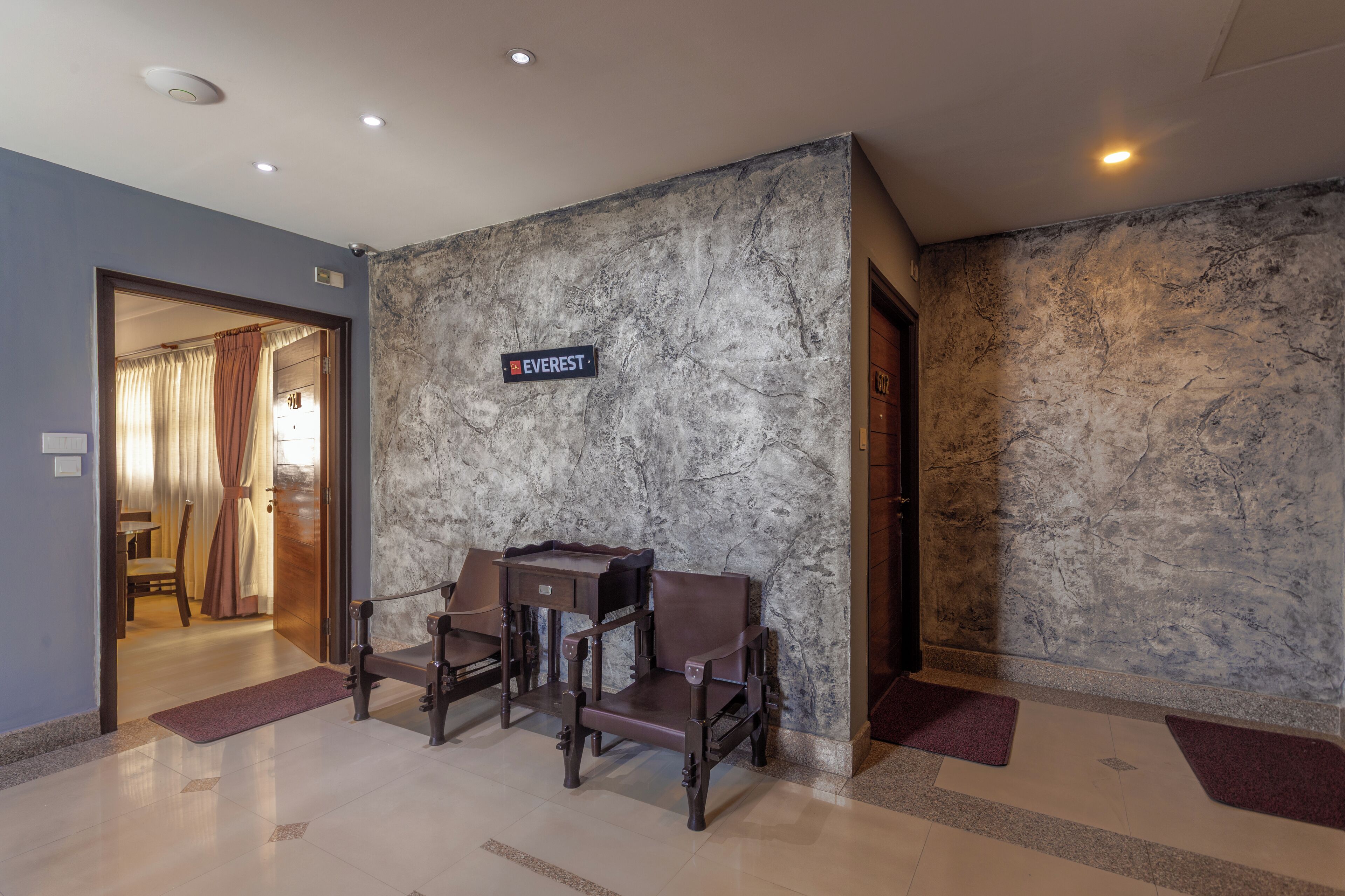 Eine Hotellobby mit einer Marmorwand, einem Schild mit der Aufschrift "EVEREST" und einer Sitzecke mit zwei Stühlen und einem kleinen Tisch.