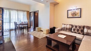 A modern living room with a wooden coffee table, a beige sofa, and a dining area with a table and chairs. - Suite Homes, Serviced Apartment Hotel (Lalitpur)