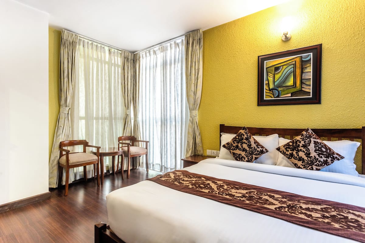 Habitación de hotel con una cama grande, cabecera de madera, un cuadro en la pared y una ventana con cortinas.