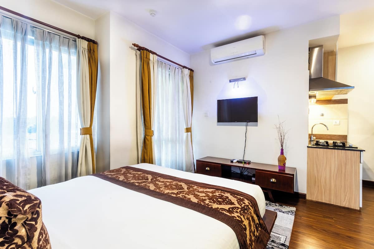 Una habitación de hotel con cama, escritorio, televisión y kitchenette.