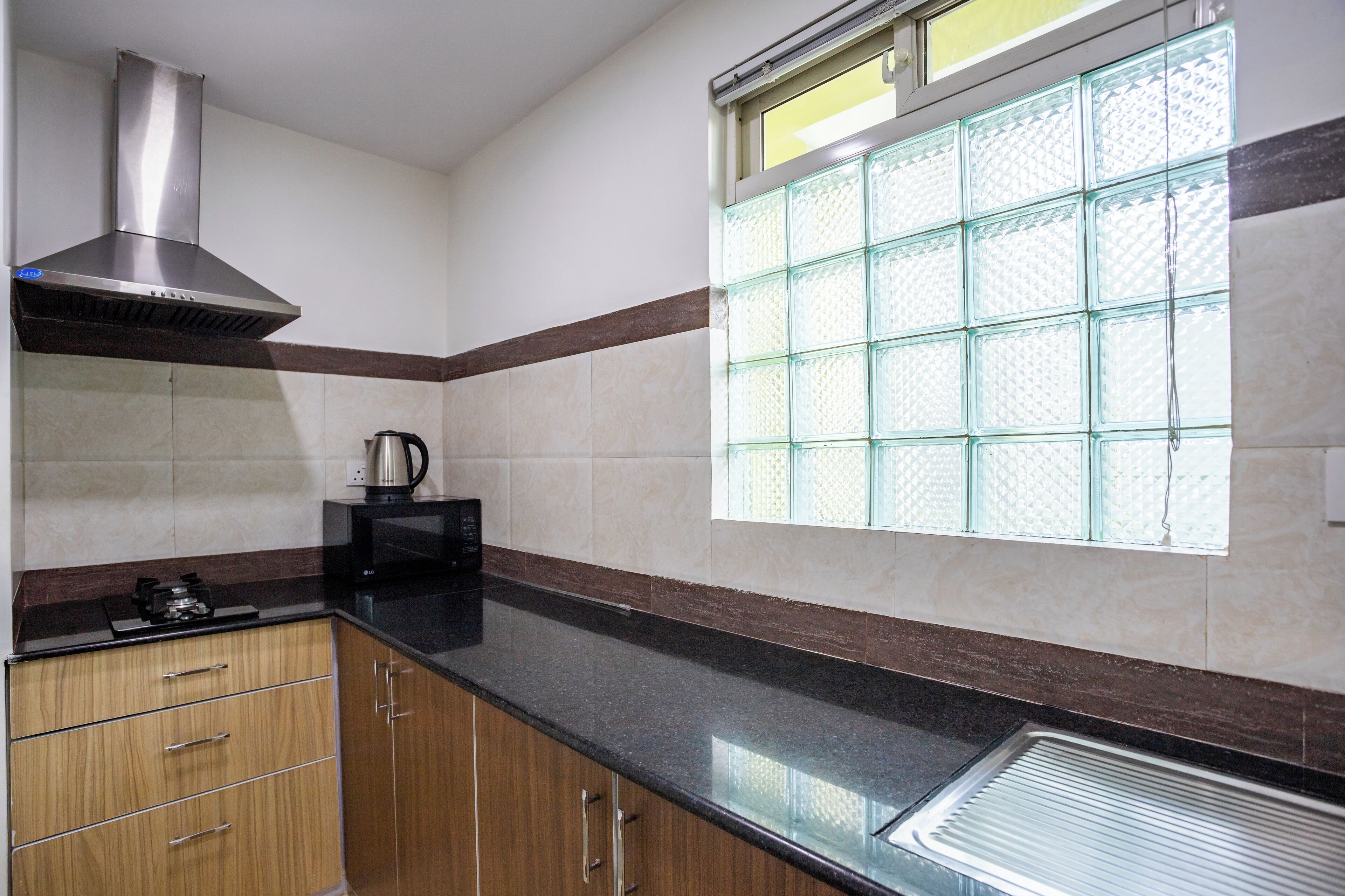 Una cocina con armarios de madera, una campana extractora de acero inoxidable, un microondas y una ventana con diseño de cuadrícula.