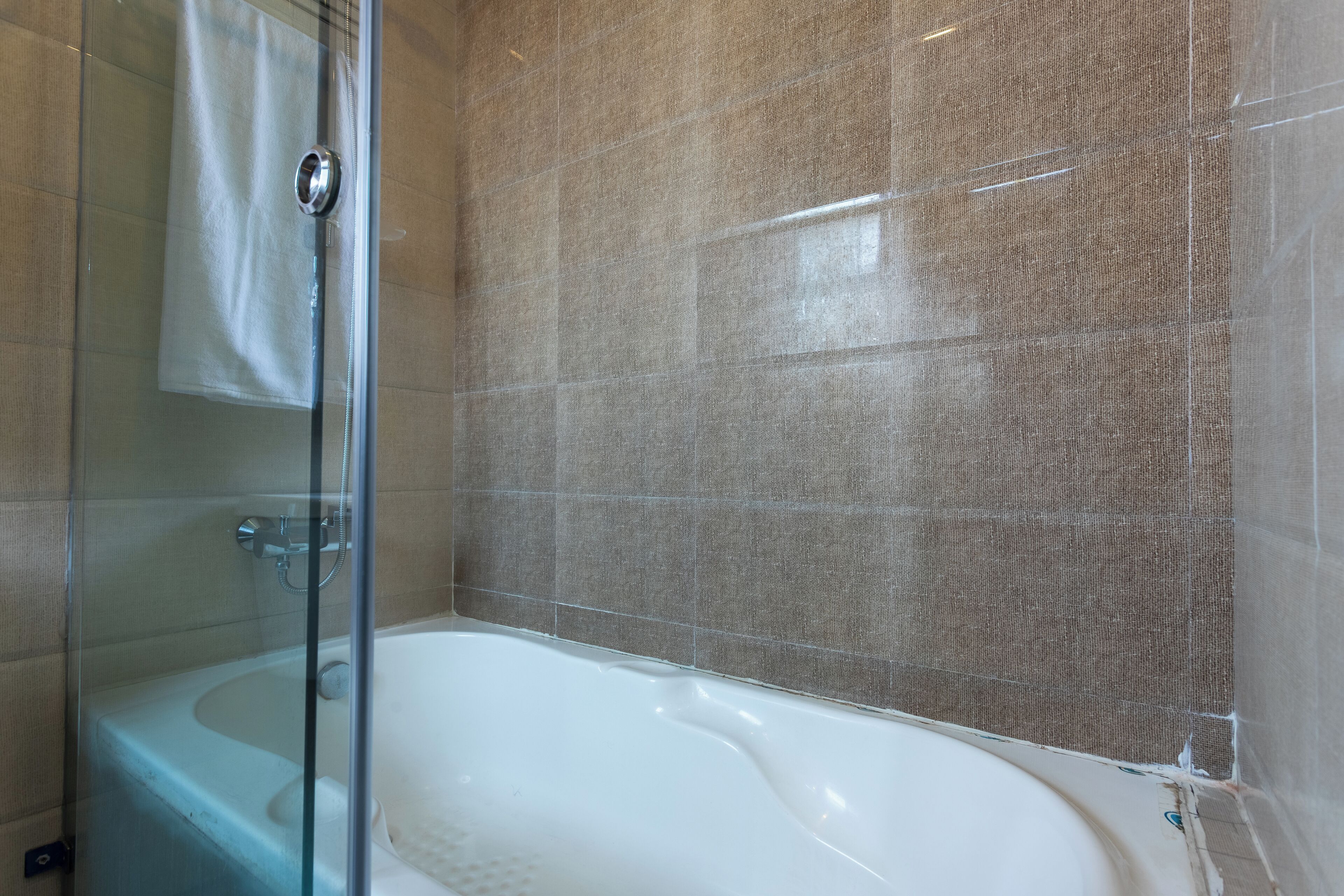 A bathroom with a glass shower enclosure, a white bathtub, and beige textured walls.
