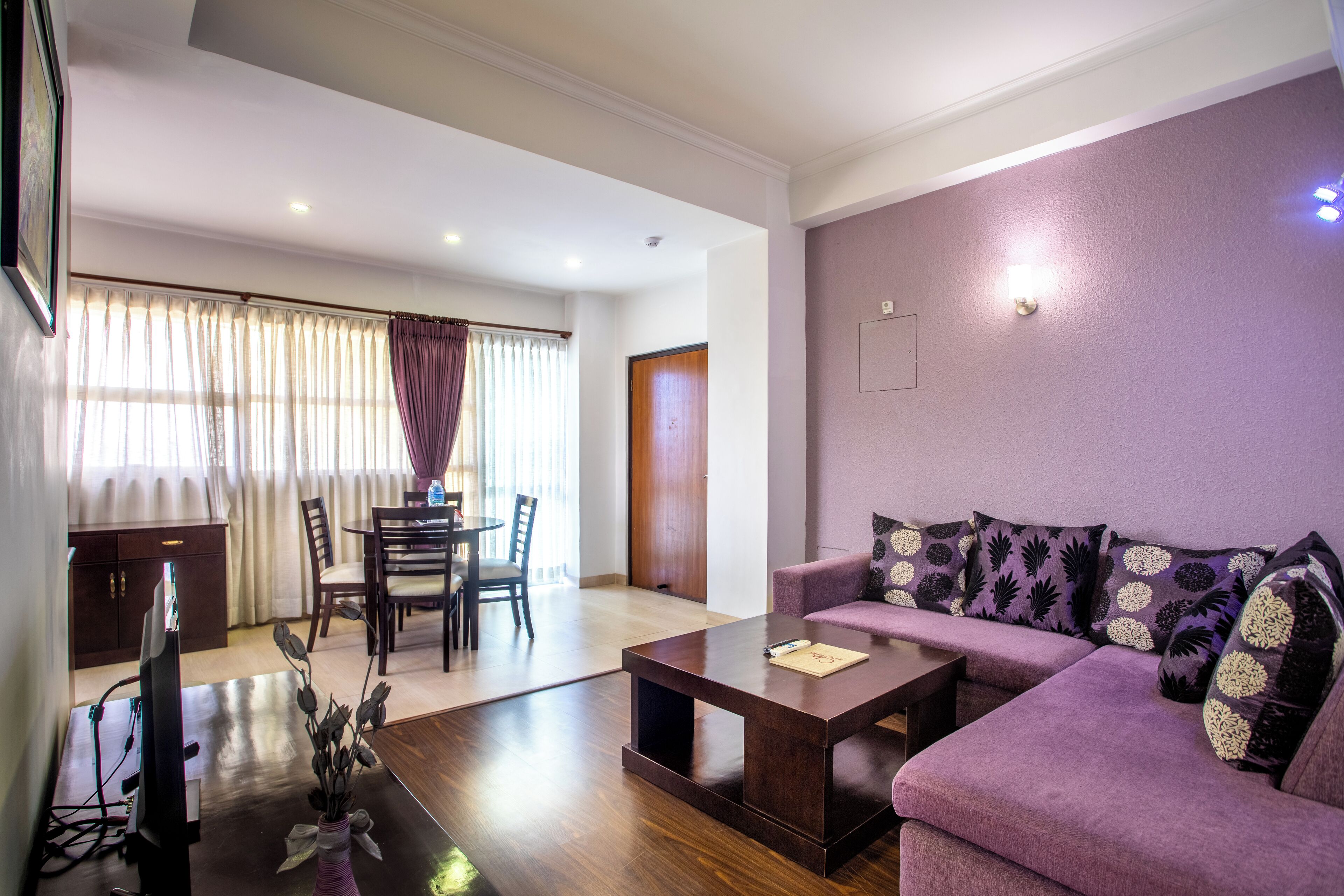 Una sala moderna con un sofá púrpura, una mesa de centro y un comedor con una mesa y sillas.