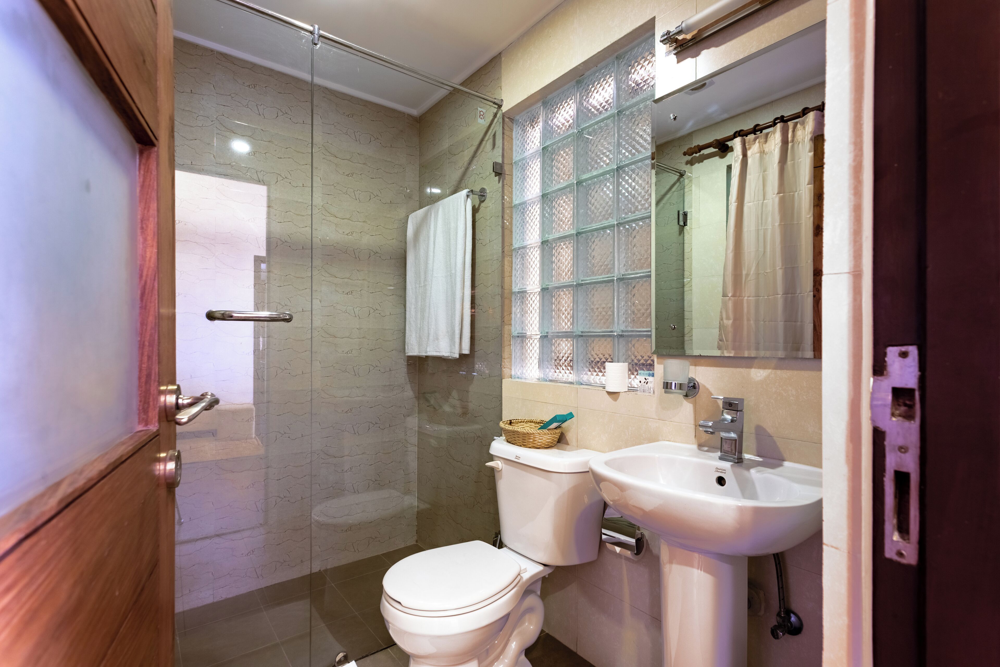 A bathroom with a glass shower enclosure, a white toilet, a sink, and a mirror with a decorative glass panel.