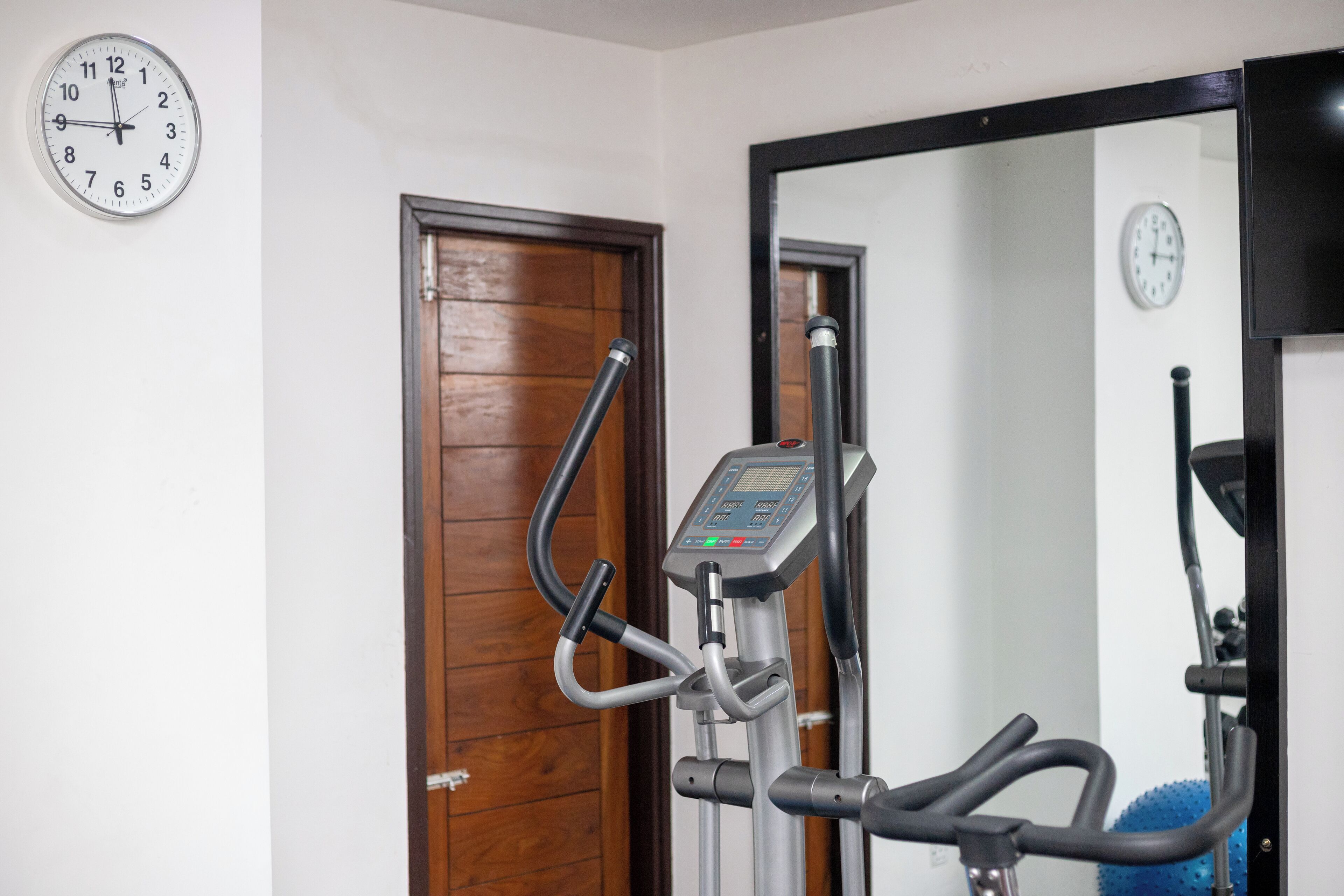 An exercise machine with a digital display, a wooden door, and a wall clock.