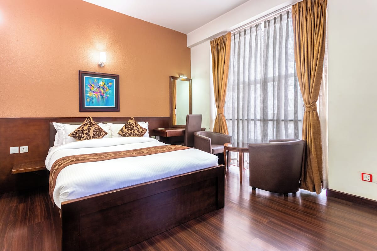 Habitación de hotel con una cama grande, un escritorio, una silla y una ventana con cortinas.