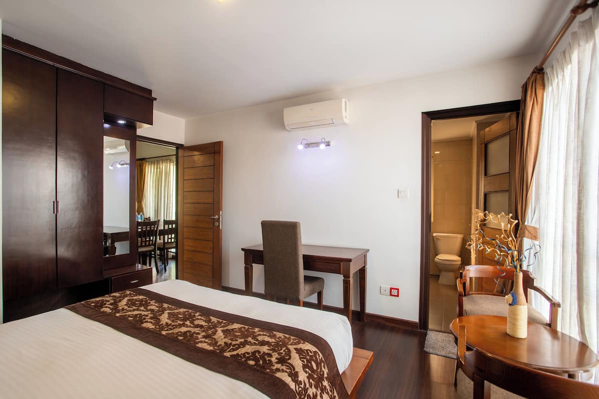 Una habitación de hotel con cama, escritorio, silla, armario y aire acondicionado.
