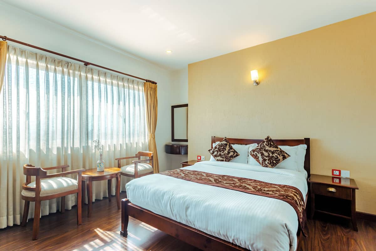 Una habitación de hotel con una cama grande, muebles de madera, un escritorio y un ventanal con cortinas.