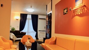 Eine Hotellobby mit orangefarbenen Sitzgelegenheiten, einem Empfangstresen, einem Bücherregal und einer Wand mit einem Blumenbild.
