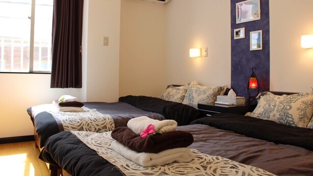 Ein Hotelzimmer mit zwei Betten, einem Fenster mit Vorhängen, einer Klimaanlage, einem Nachttisch mit Lampe und Wandleuchten.