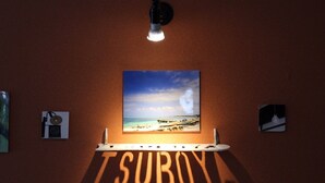 Eine Wand mit einem gerahmten Foto vom Strand, einer Lampe und dem Wort 'TSUBOYA' im Schatten.