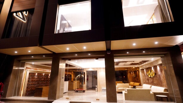A modern hotel entrance with a reception desk, seating area, and a glass elevator. - Hotel City Pride (New Delhi)