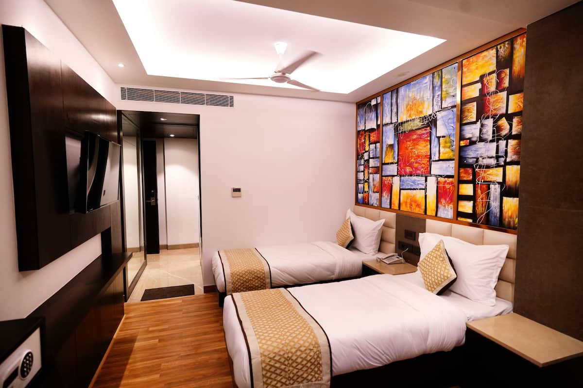 Une chambre d’hôtel avec deux lits, un ventilateur de plafond, un grand tableau abstrait et un téléviseur fixé au mur.