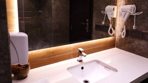 A modern bathroom with a large mirror, white sink, and two hair dryers mounted on the wall. - Hotel City Pride (New Delhi)