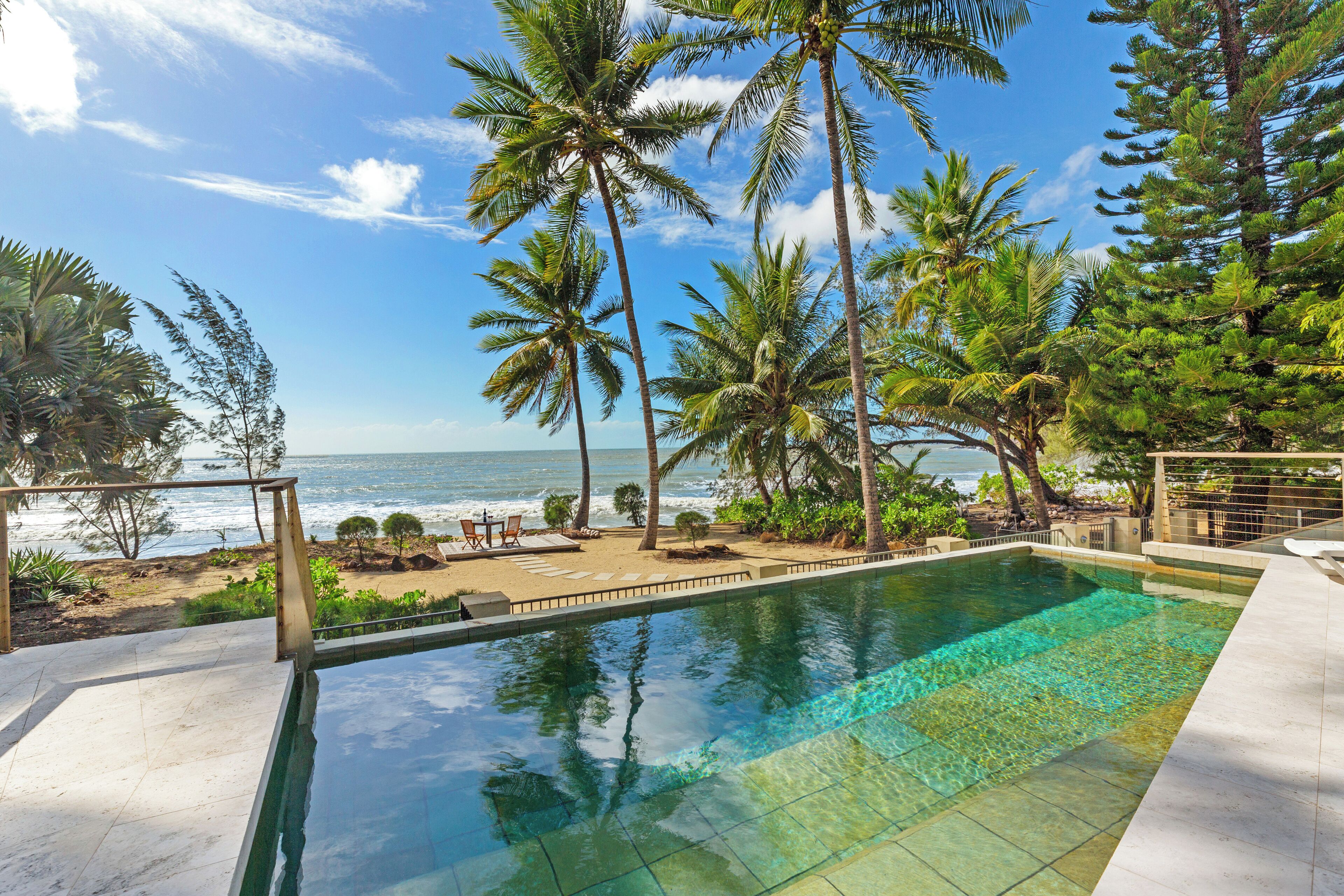 A clear view of a swimming pool with a beach and ocean in the background.