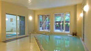 An indoor swimming pool with clear glass walls, a tiled floor, and a metal pool ladder. - Hotel Hananoki (Nikko)