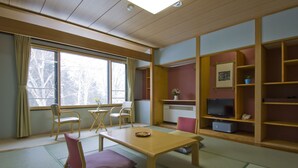 A room with tatami mats, a wooden table, chairs, a TV, and a shelf with items. - Hotel Hananoki (Nikko)