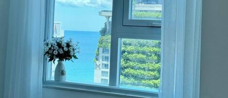 A room with a large window offering a view of the sea and buildings.