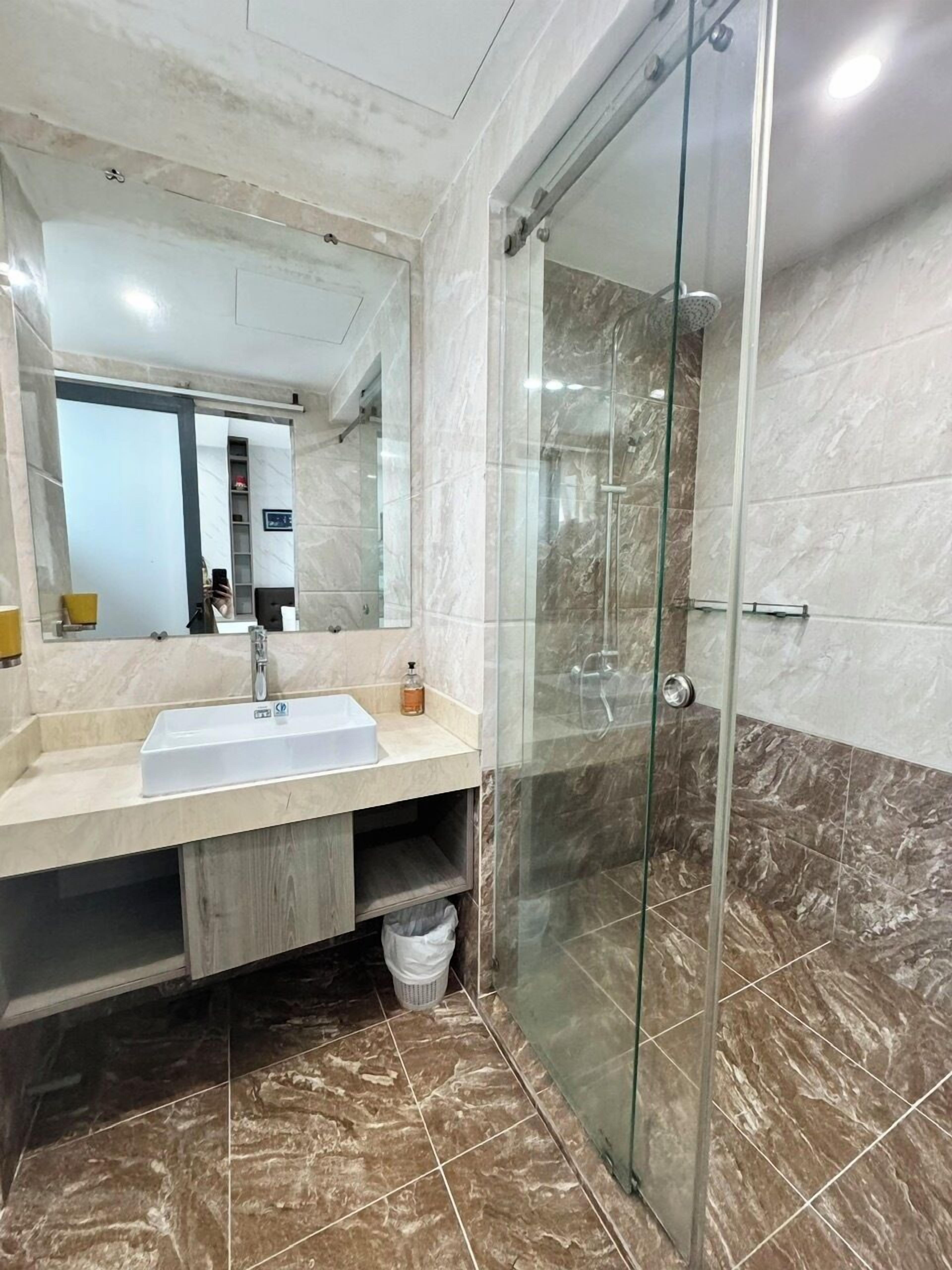 A modern bathroom with a large mirror, a sink, and a glass-enclosed shower.