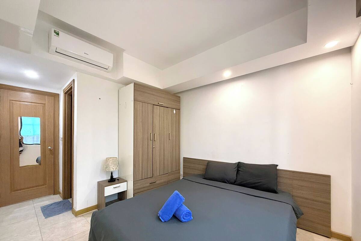 A hotel room with a bed, a wardrobe, a nightstand, and an air conditioning unit.