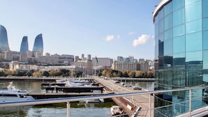 Ein Yachthafen mit vertäuten Booten, ein modernes Glasgebäude und eine Stadtansicht mit markanter Architektur im Hintergrund.