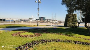 A park with flower beds, a lamp post, and a view of a marina with boats and buildings in the background.