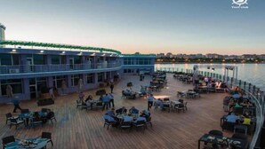 Ein stilvoll eingerichtetes Restaurant mit Außenbereich und Blick auf ein Gewässer, im Hintergrund die Skyline einer Stadt.
