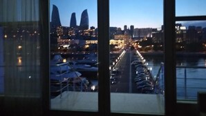 Blick aus einem Fenster eines Hochhauses auf eine beleuchtete Stadtlandschaft im Abenddämmerung, mit einem belebten Straßenbild.