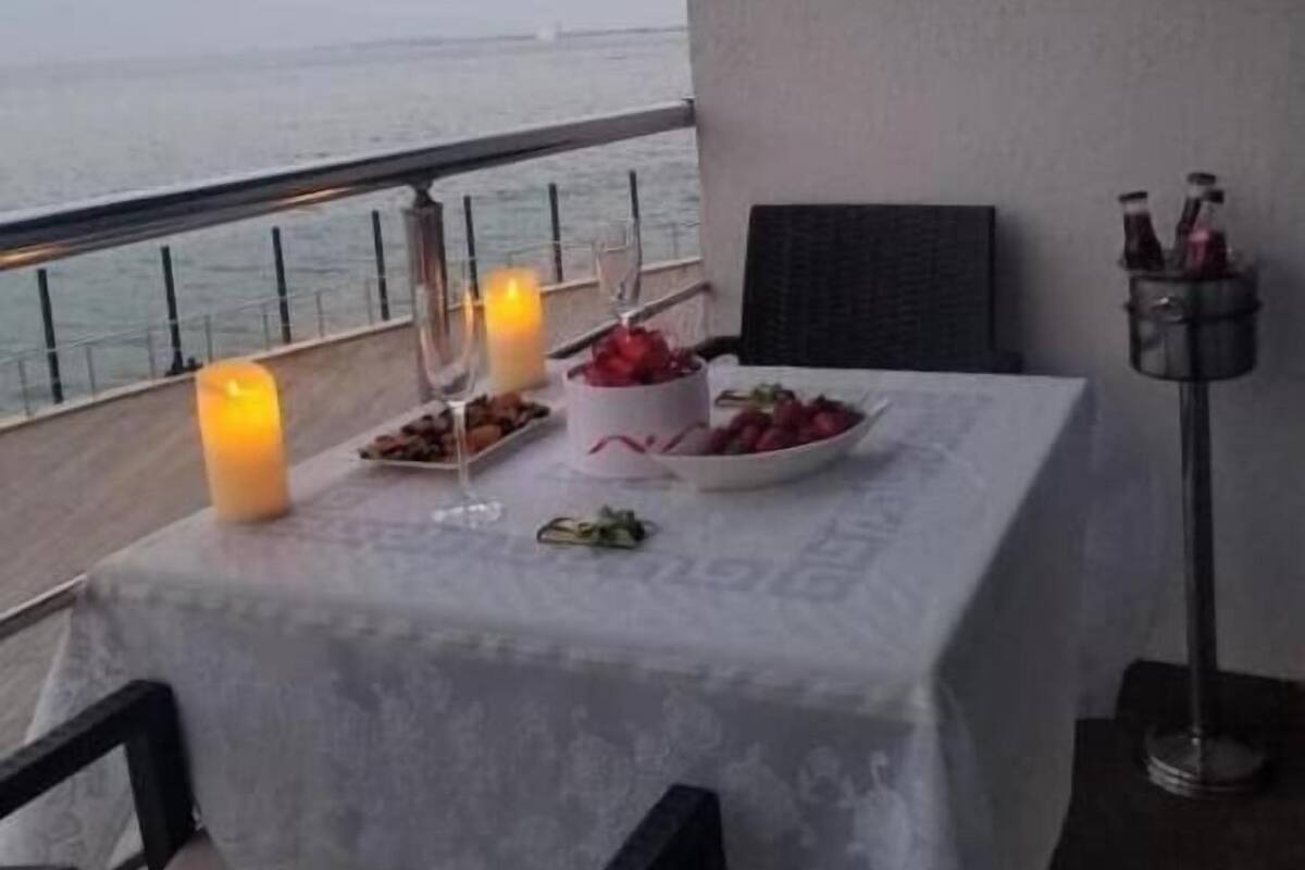 Una mesa dispuesta con velas, frutas y copas en un balcón con vista al mar.