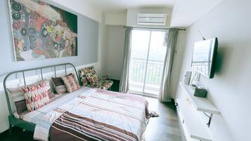 A bedroom with a bed, a painting, an air conditioner, a TV, and a balcony with curtains.