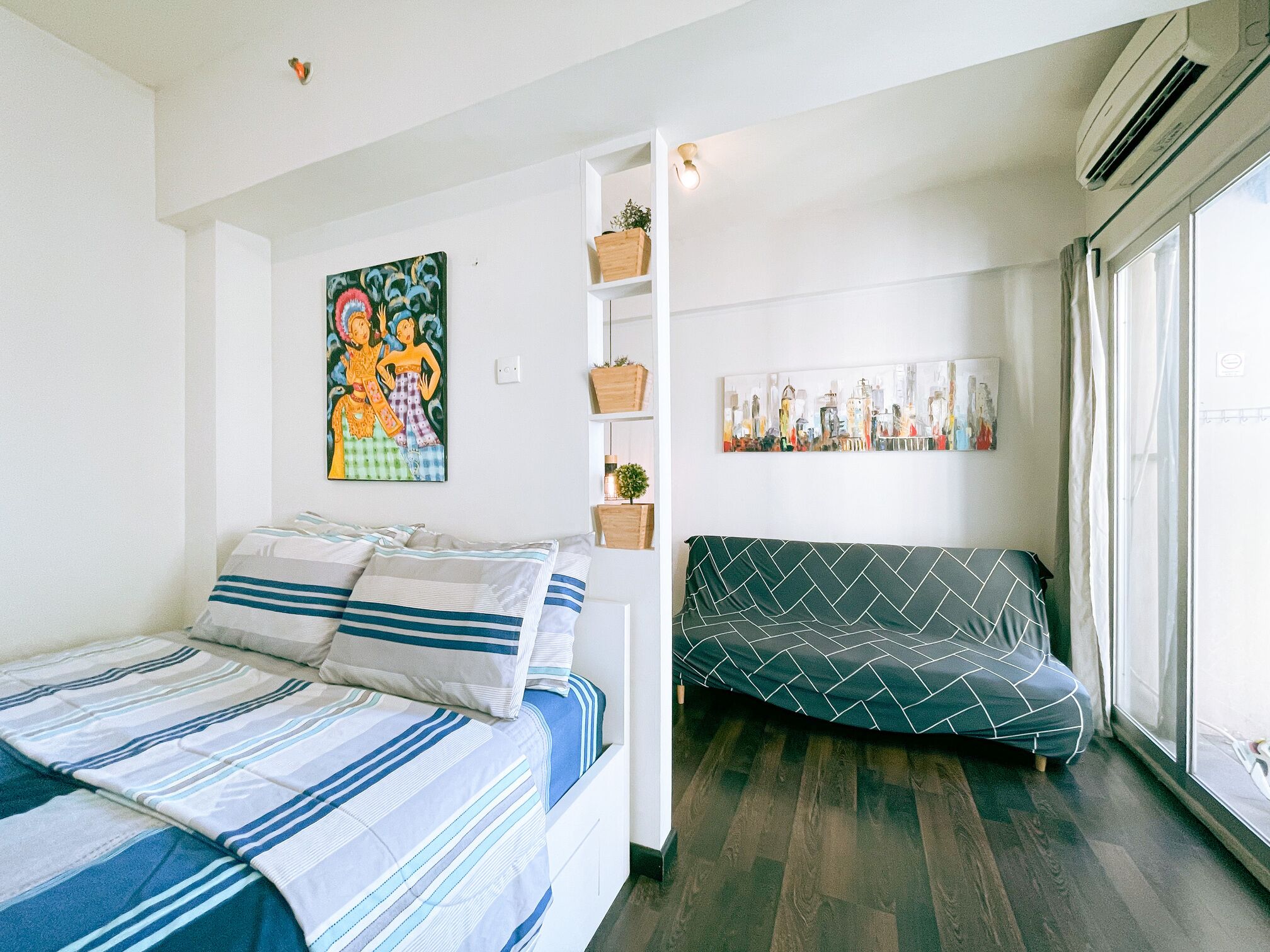 A modern bedroom with a bed, a sofa, and a cityscape painting.