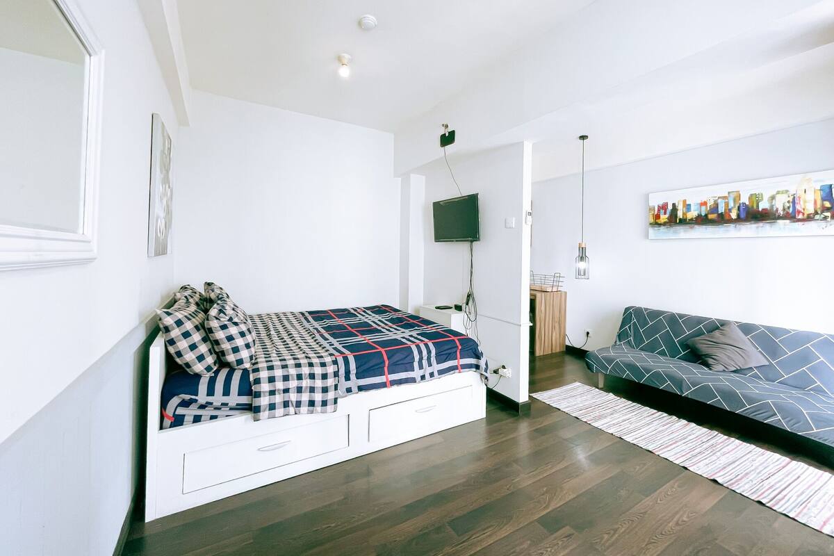 A bedroom with a bed, a TV, a sofa, and a painting on the wall.