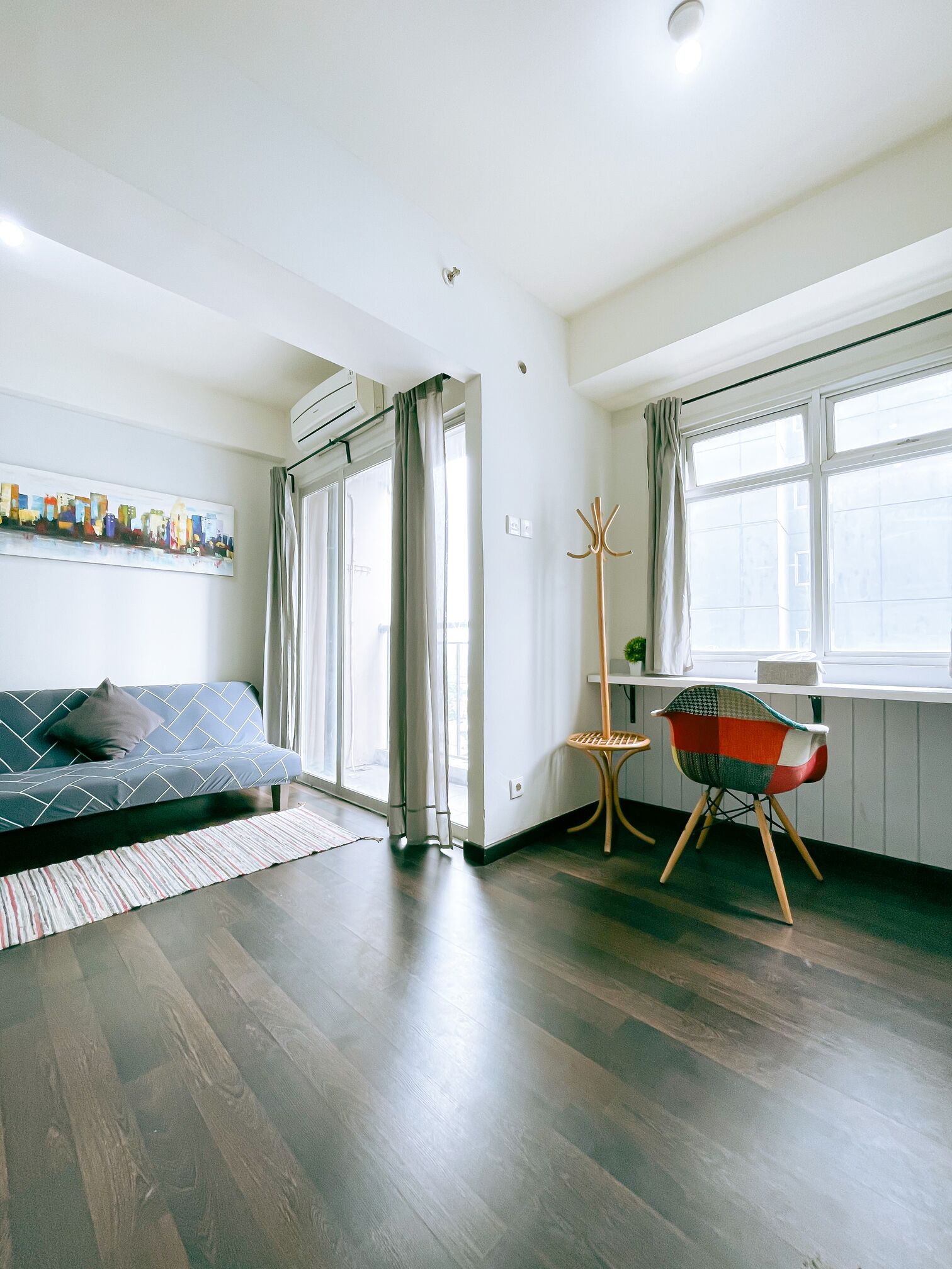 Una sala de estar moderna con un sofá, un sillón colorido, un perchero y un ventanal grande.