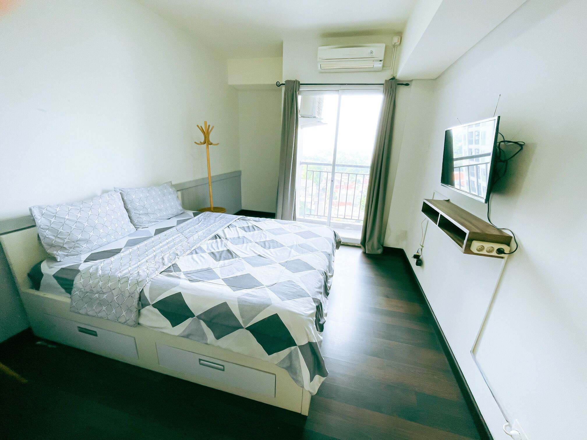 Un dormitorio con cama, aire acondicionado, televisor y ventana con cortinas.