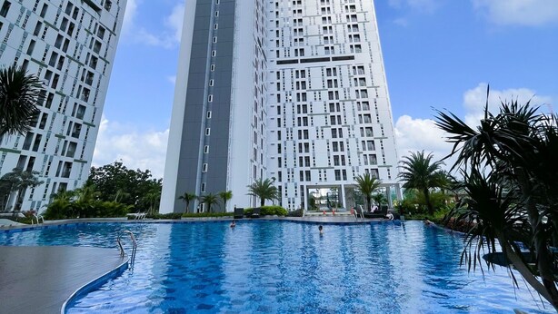 A swimming pool surrounded by modern high-rise buildings. - The Satu Stay Apartement SGV (South Tangerang)